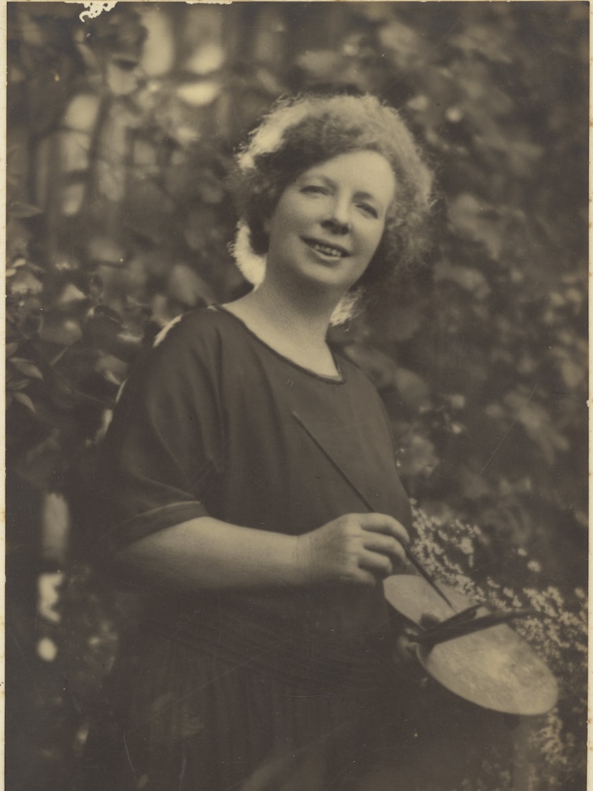 Black and white image of Margaret Preston standing in a garden holding a paint palette