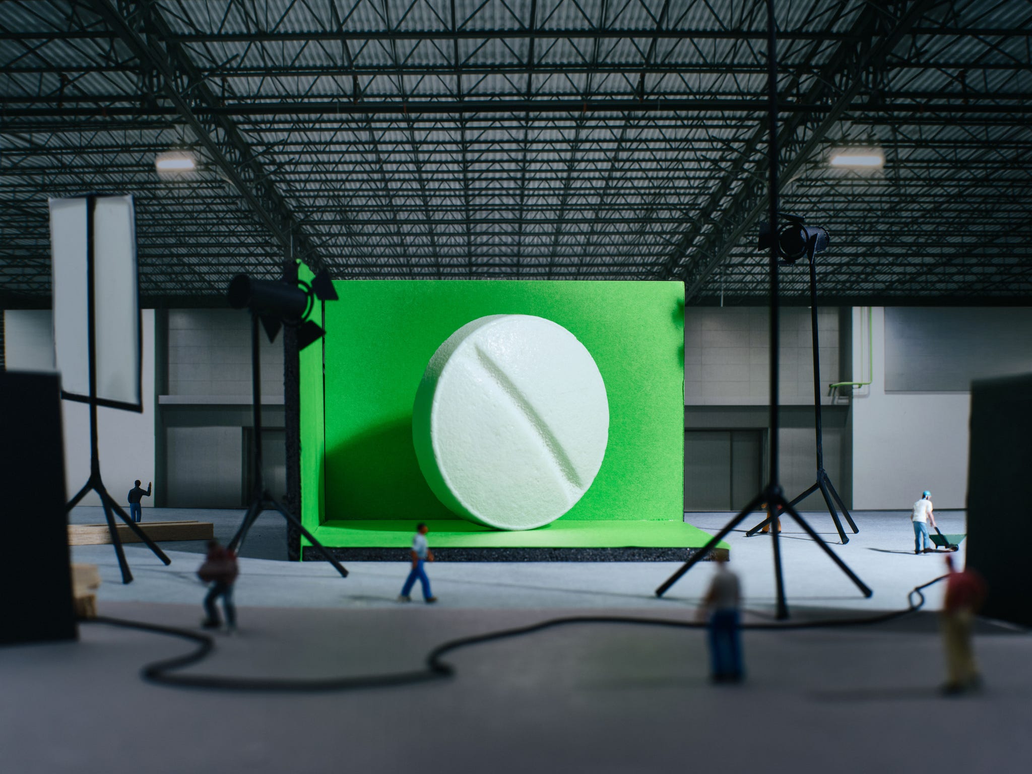 Miniature figures working on a film set featuring a large pill against a green backdrop.