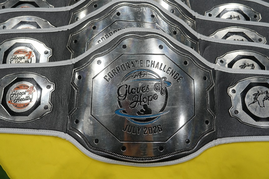 A number of shiny trophy belts lined up on a table, they feature the Hoops 4 Health logo alongside the words: Gloves of Hope