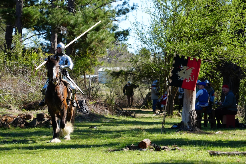 A soldier on horseback rides past a flag and group of soldiers 