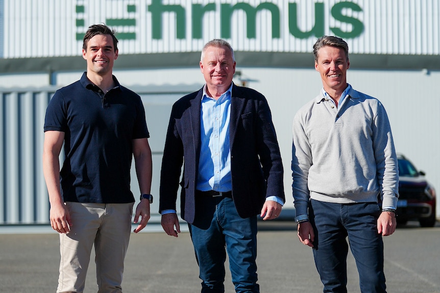 Three men standing outside a building that says 'Firmus'.