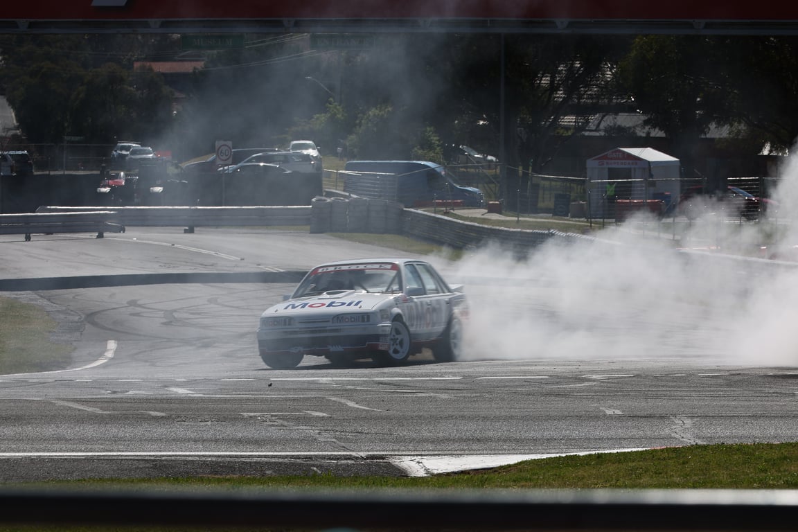 White Mobil-branded Brock race car doing a smoky burnout on a racetrack.