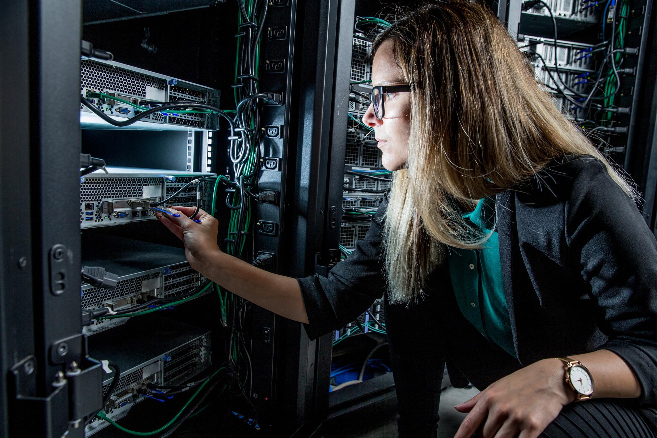 A data center engineer is checking wires and switches on an enterprise server tower.