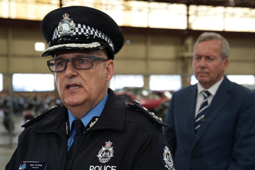 Mike wears his police uniform while standing in front of Reece Whitby at a press conference