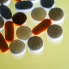 A close-up photo of various over-the-counter pain medicines, including Tylenol, Aspirin, Ibuprofen and Aleve, on a yellow background, hit from behind.
