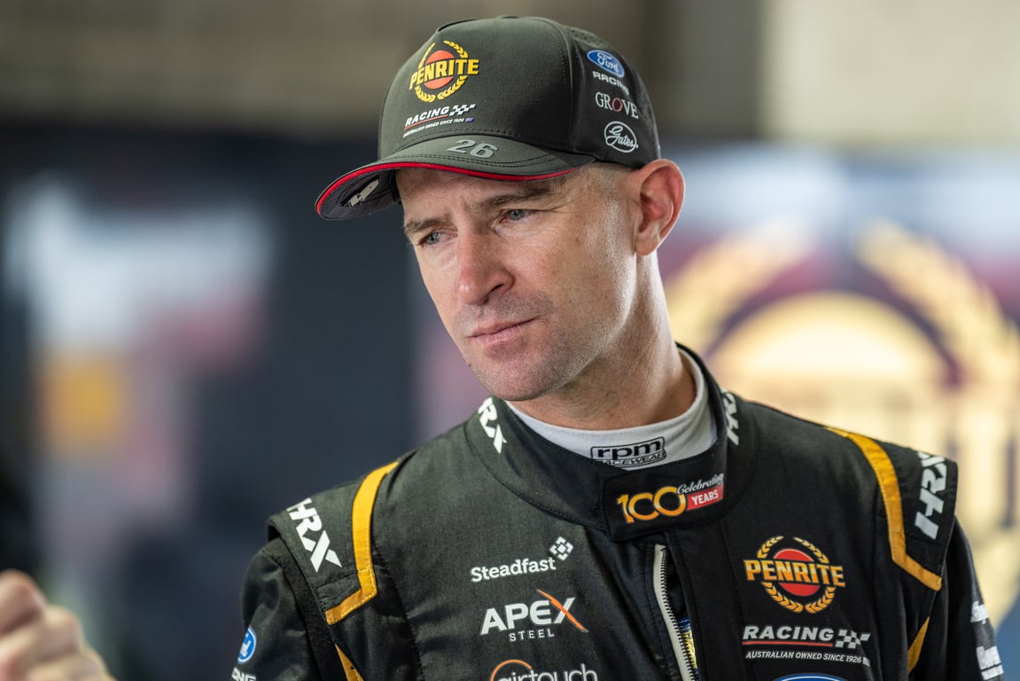Will Davison in Penrite Racing cap and suit looking to the side in the paddock.