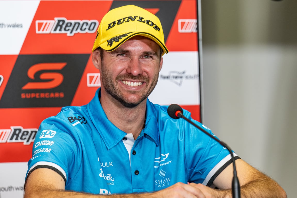 Aaron Seton smiling in a yellow Dunlop cap at a press conference with Repco branding behind him.