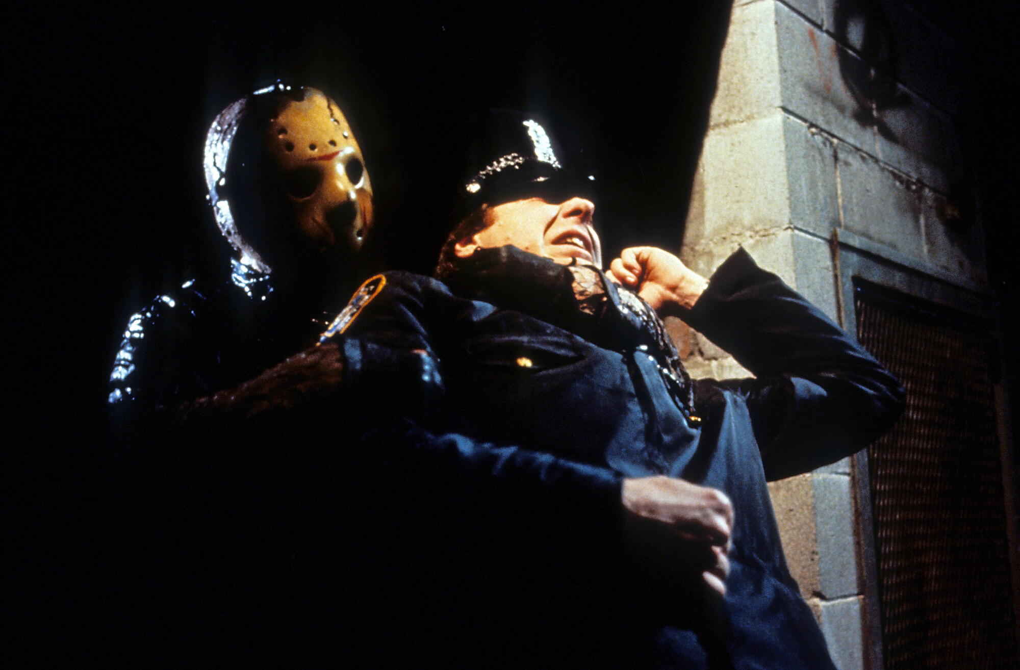 A man in a hockey mask grabs a cop around the neck.