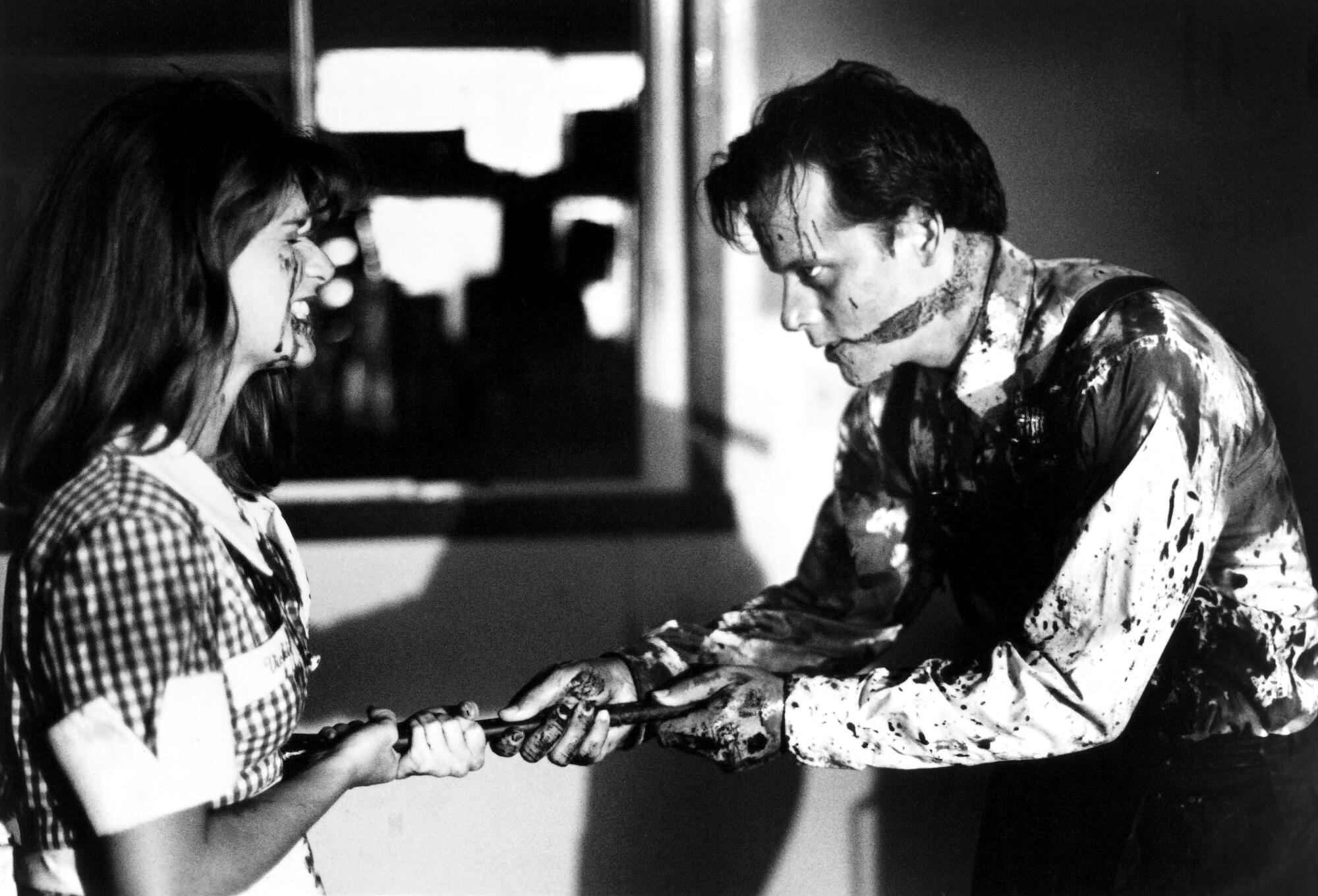 A black and white photo of a woman struggling with a man covered in blood.