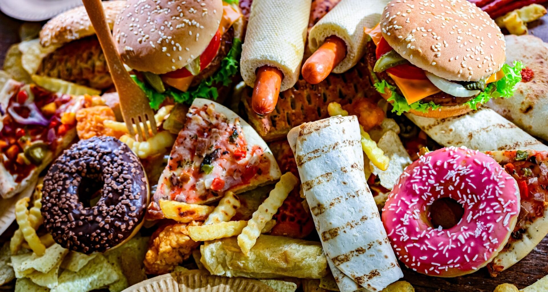 Assortment of ultraprocessed foods, including burgers, hot dogs, pizza, fries, and colorful doughnuts.