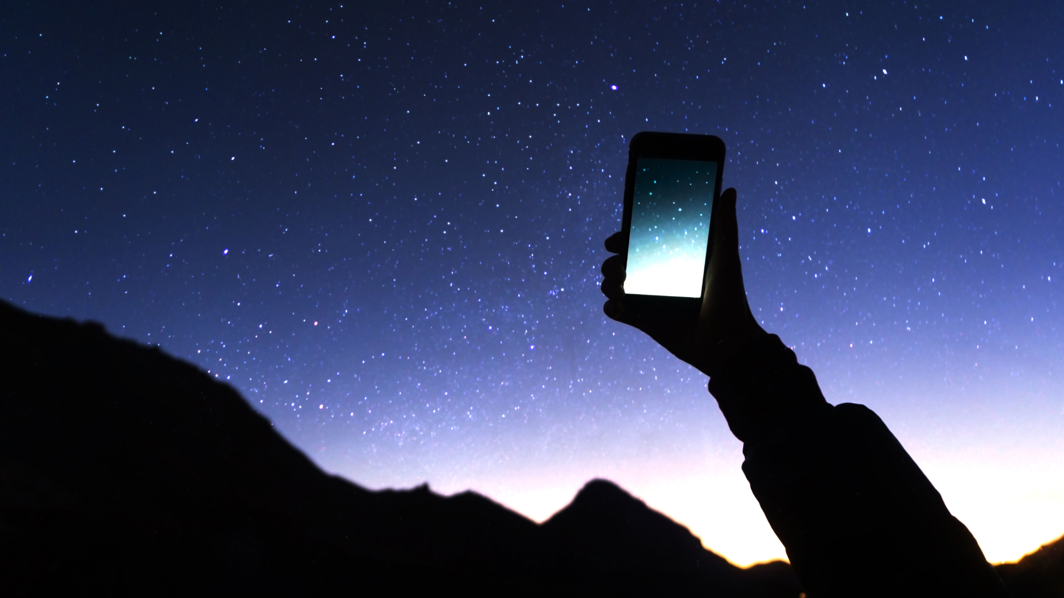 Image shows person holding mobile up to starry night sky