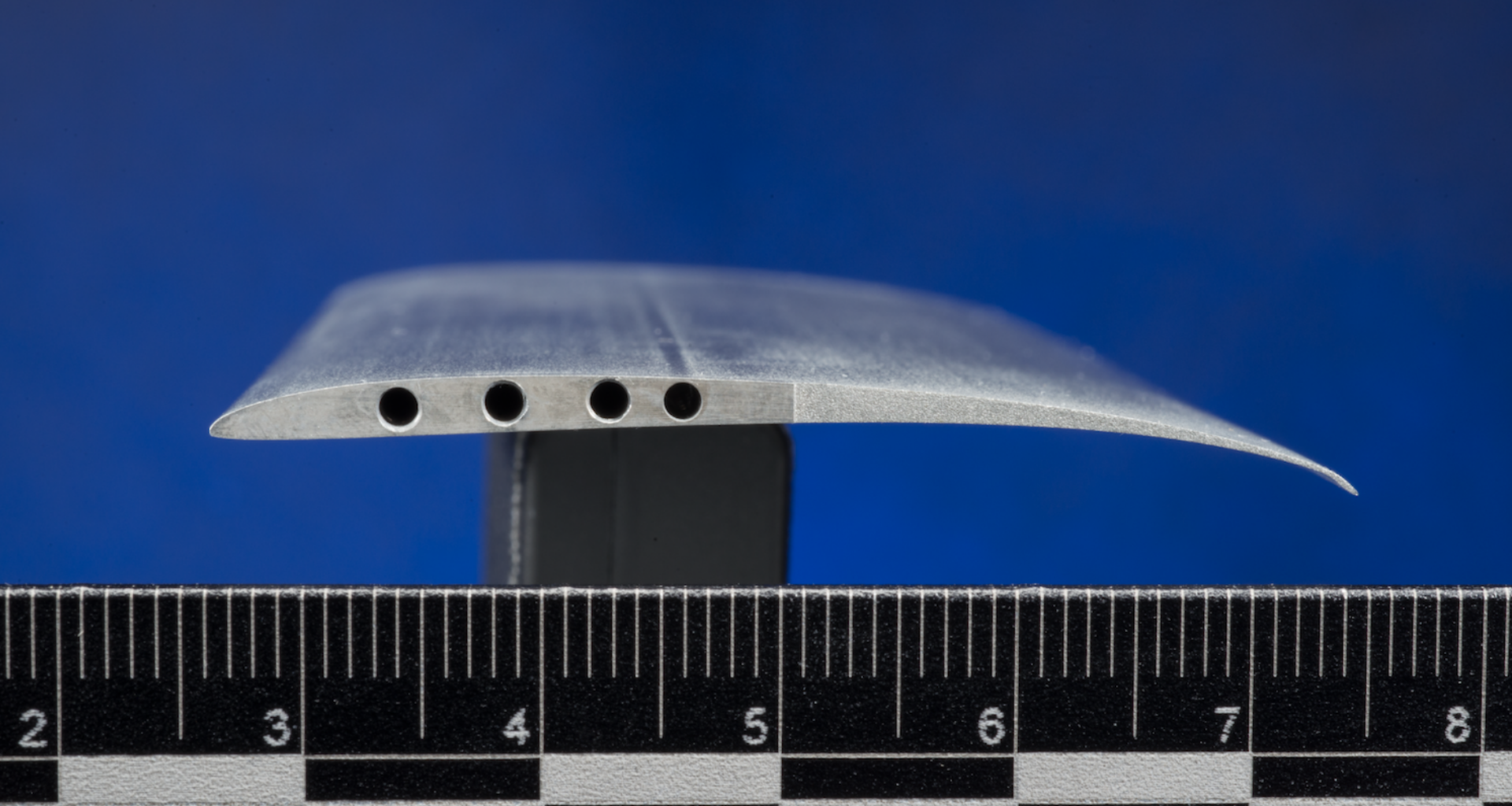 A close-up view of a cross-section of the Ingenuity rotor blade, also called an airfoil. The blade is shaped like an arched teardrop with holes drilled into the side.