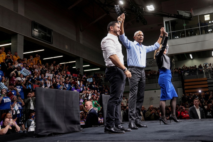 Barack Obama on a stage with Abdul El-Sayed, raising their arms to the crowd