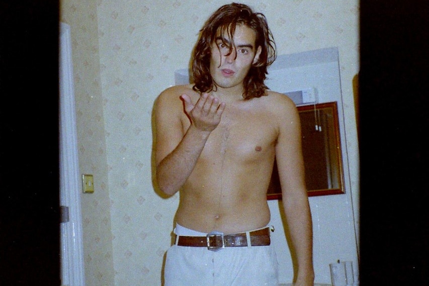 A man wearing trousers and no shirt blowing a kiss at the camera.