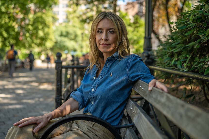 A woman with blonde hair wearing a blue shirt sitting on a park bench.