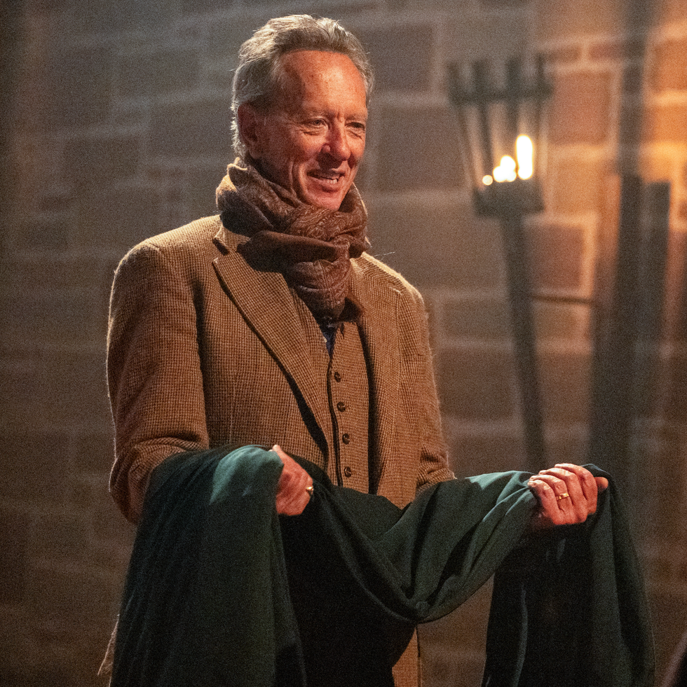 person smiling warmly indoors, holding a green coat.