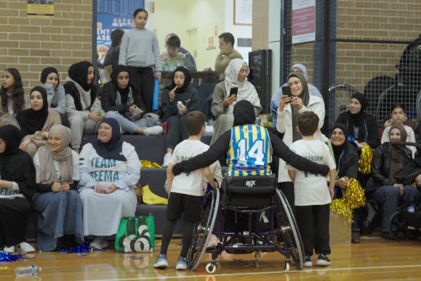 Reema El Qassem, wearing a hijab, has her arms around two young supporters as she faces people in the stands.
