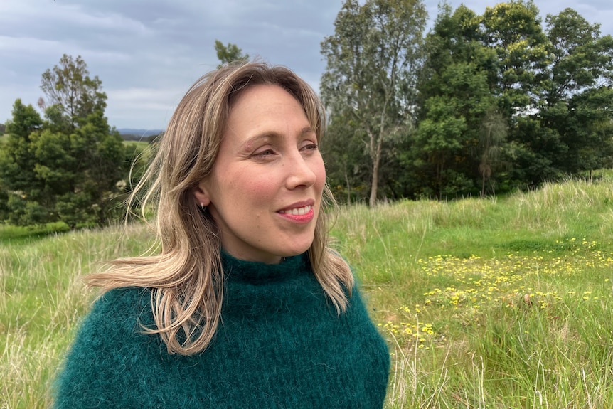 a woman in a green paddock smiles off into the distance