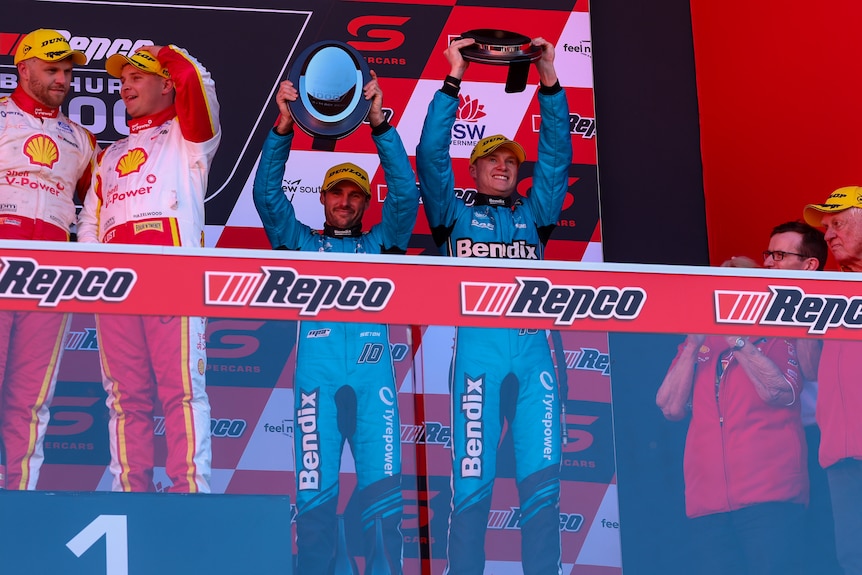 Five people stand celebrating on a motorsports podium.