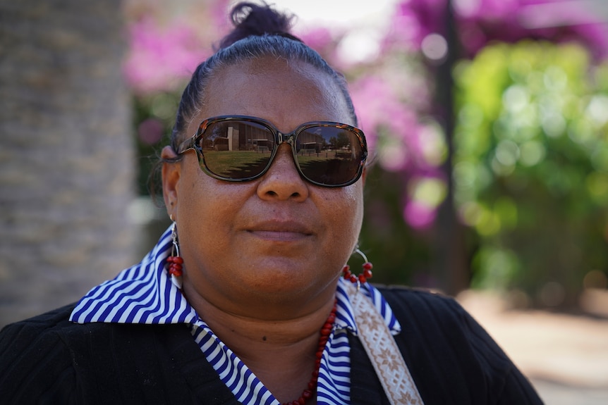 Linda Lechleitner looks directly at the camera wearing sunglasses and a blue and white striped shirt under a black jumper.