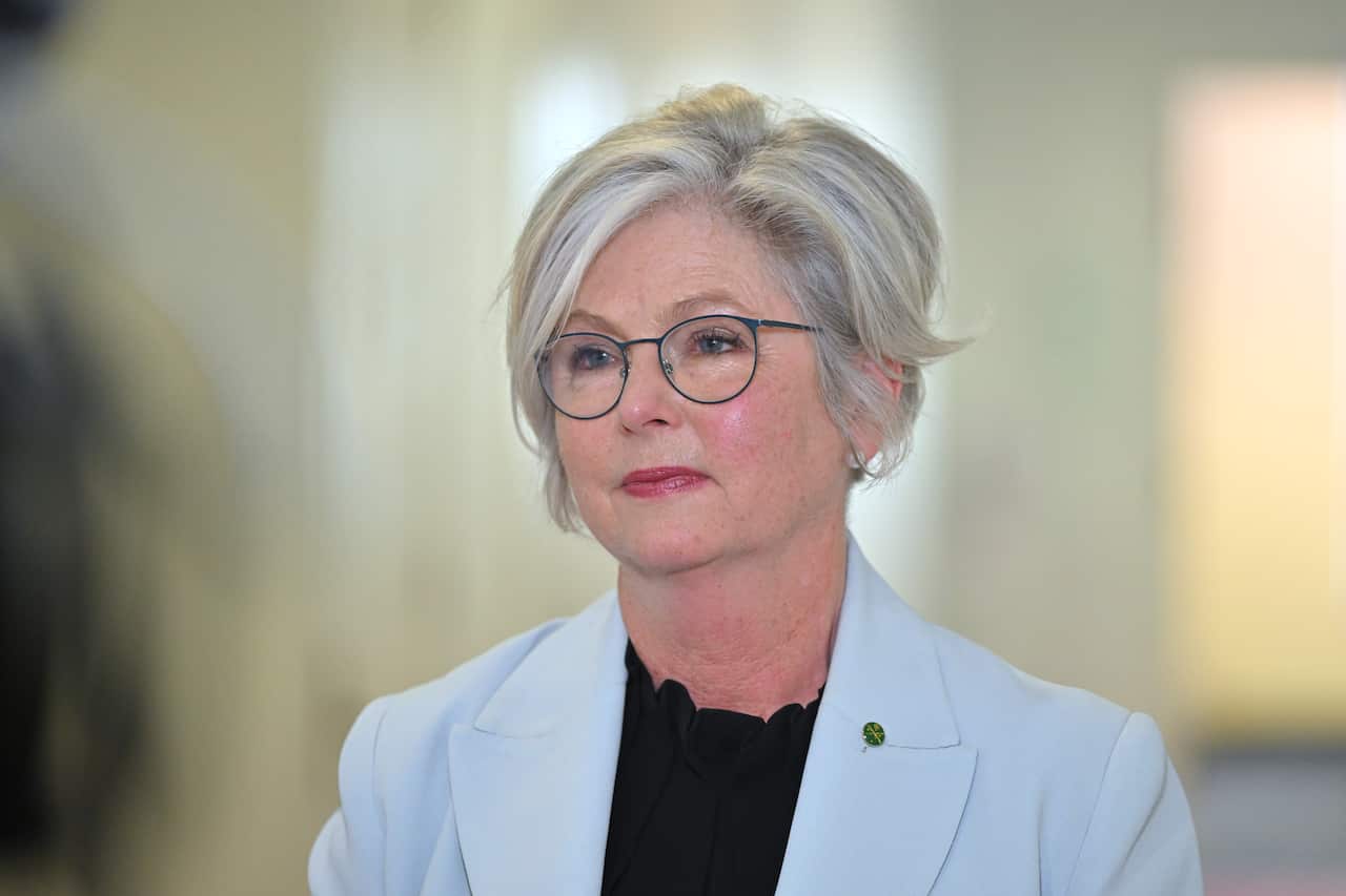 A woman with short grey hair and an aqua blue blazer smiles.