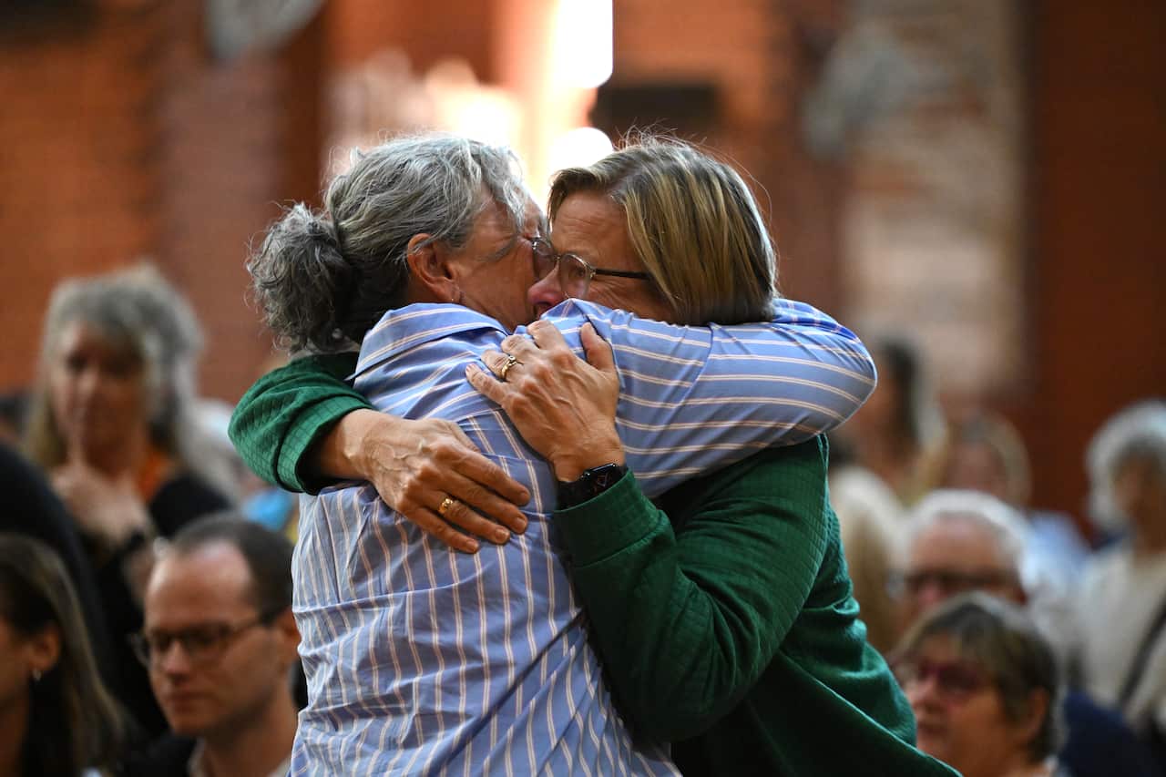 Two women embrace, one in a striped blue shirt and the other in a green cardigan 