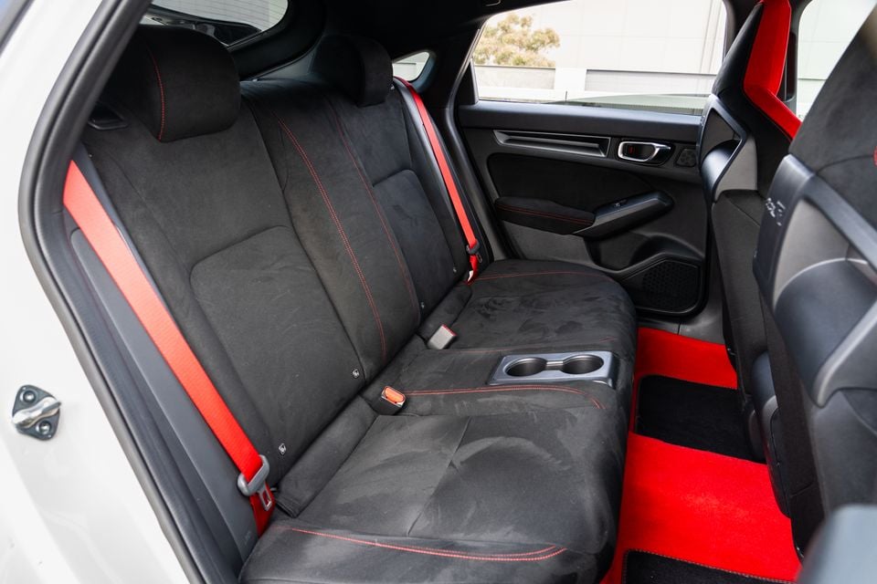Rear interior of a Honda Civic Type R showing black Alcantara rear seats with red stitching, red seat belts, and red floor mats