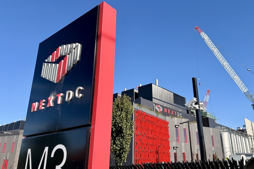 Large sign reading NEXTDC outside a large industrial building with a construction crane in the background
