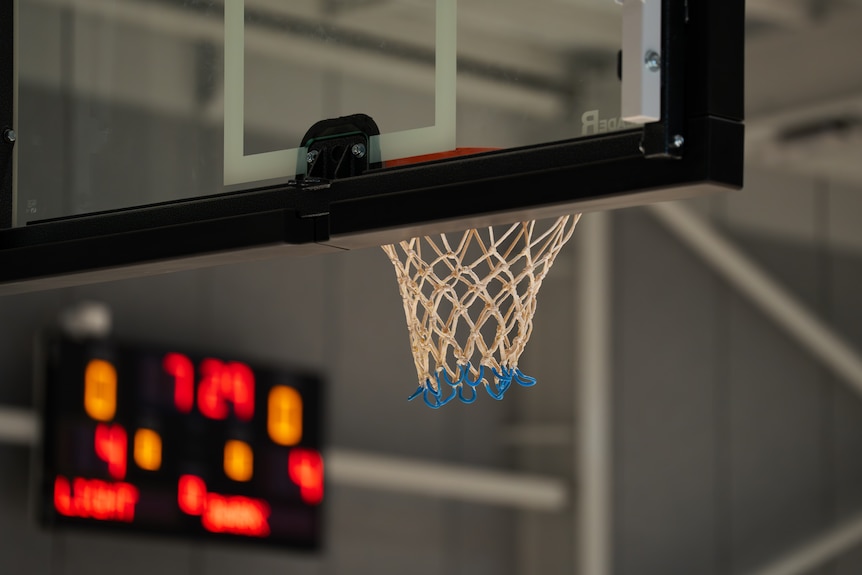 A basketball net with a scoreboard out of focus in the background