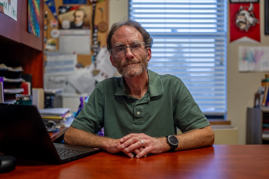 McQuide rests two hands on an office desk.