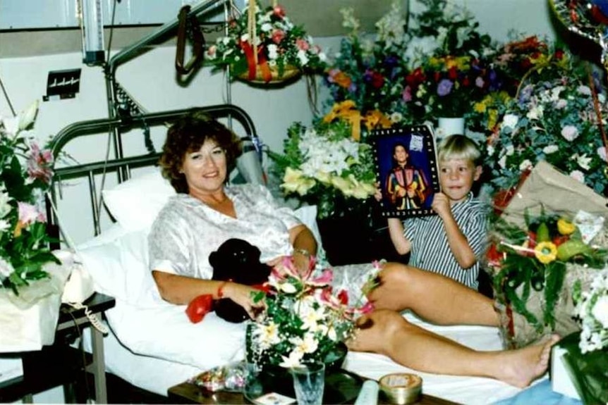 A woman sits in a bed surrounded by flowers with a small boy.
