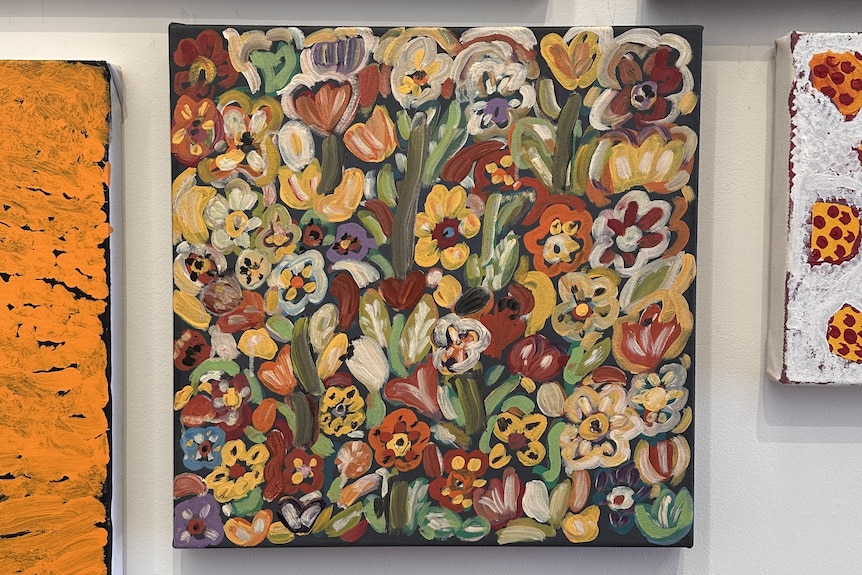 A painting of a range of colourful flowers with acrylic paint on a canvas hung on a wall.