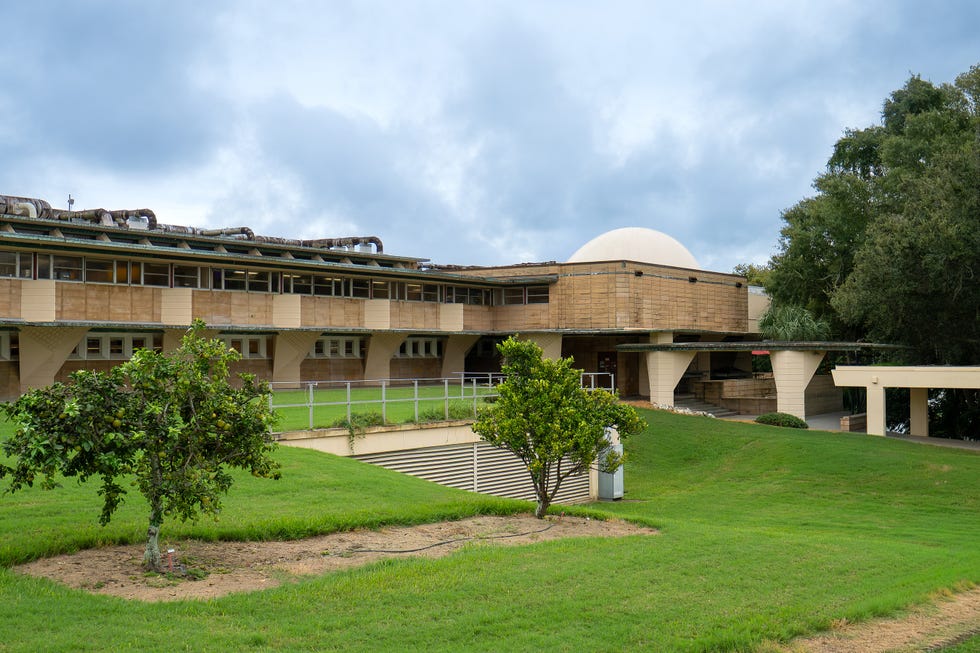 Modern architectural building with a dome, surrounded by greenery and blue sky.