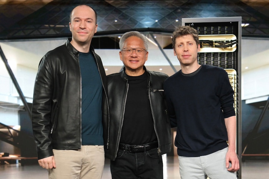 Greg Brockman, Jensen Huang and Sam Altman stand shoulder to shoulder and smile for a group photo.