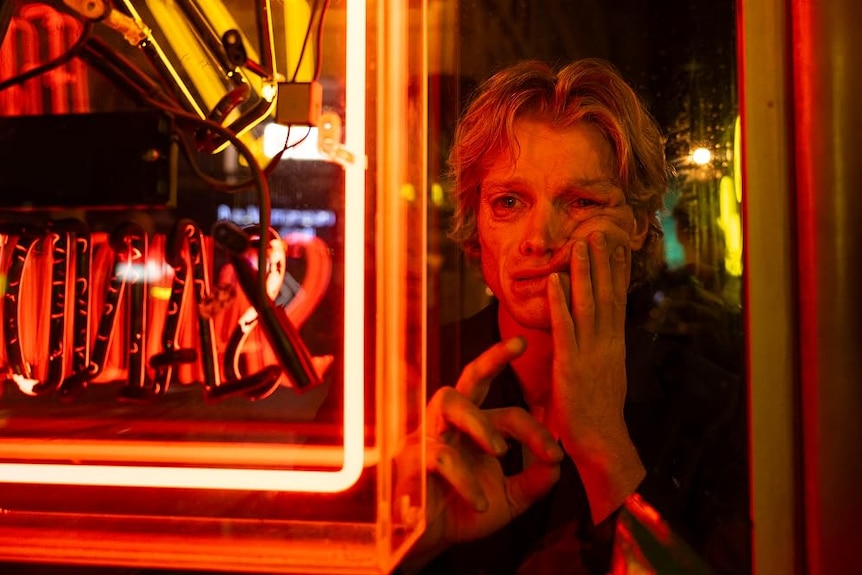 A man looks through a window at a neon sign