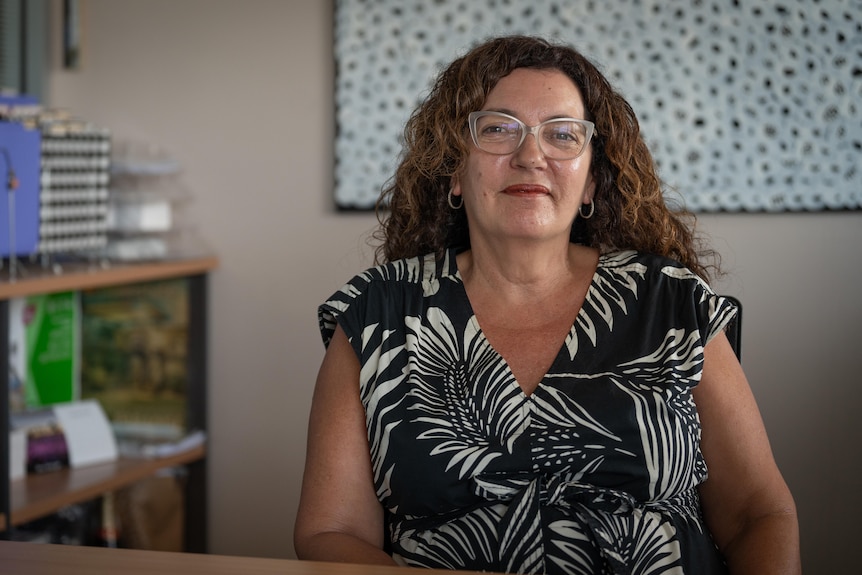 A woman with curly hair, Kerri-Ann Laurence, sits in her office and smiles at the camera.