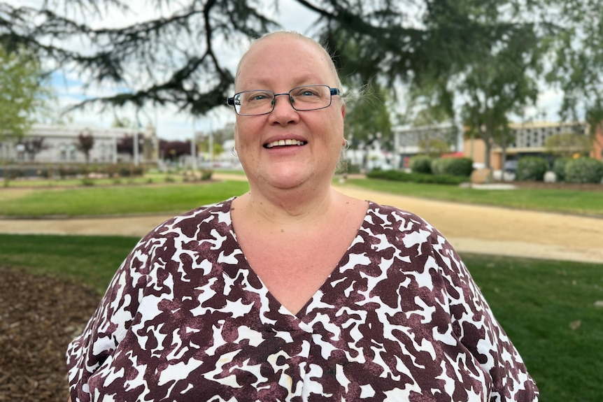 A woman in a brown and white patterned t-shirt stands in a park in central Wagga Wagga. 
