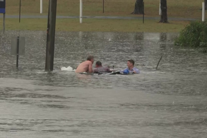 three men on top of a sinking car in floodwaters