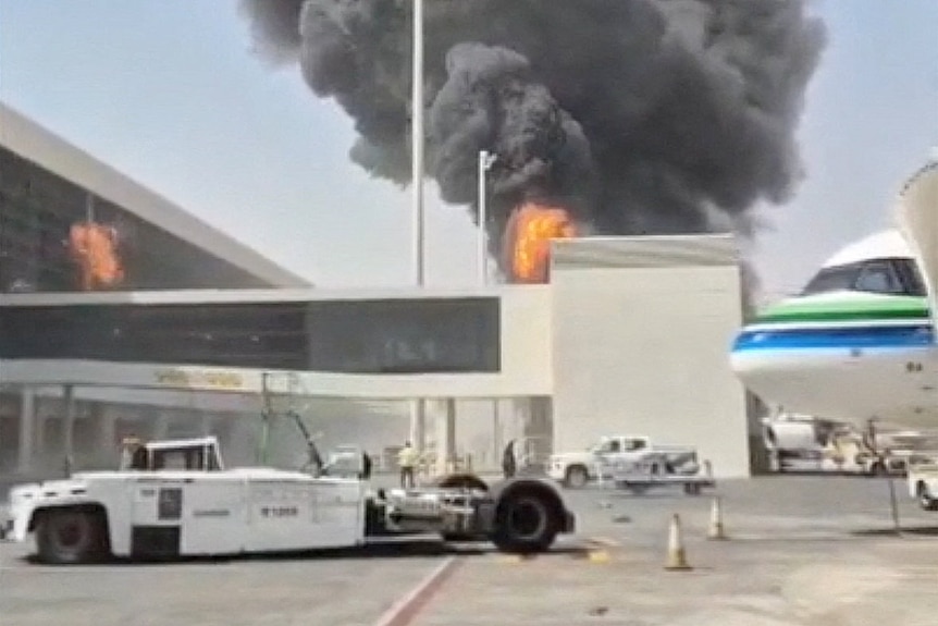 A blurry image shows a plume of smoke and fire behind an airport building.
