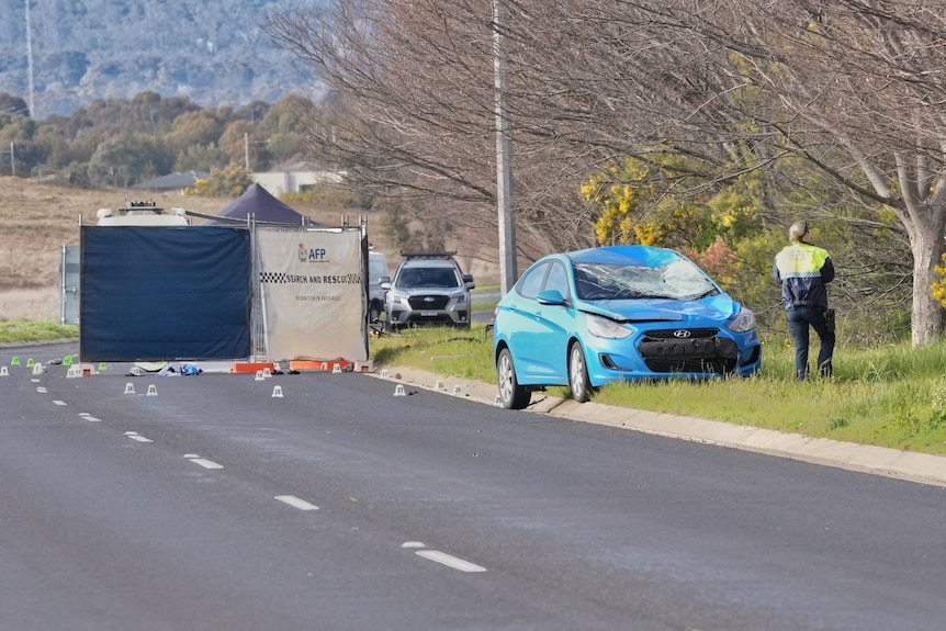A car with smashed windscreen near large screen on road blocking treatment area.