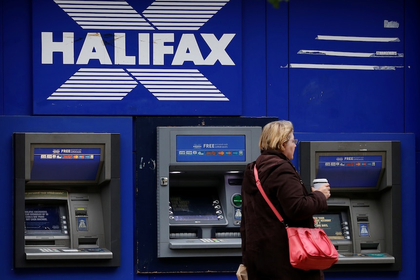 A woman walking past three Halifax ATMs.