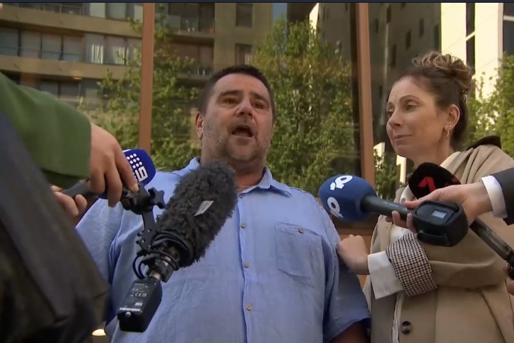 A man in a blue shirt and a woman in a trench coat speak to the media