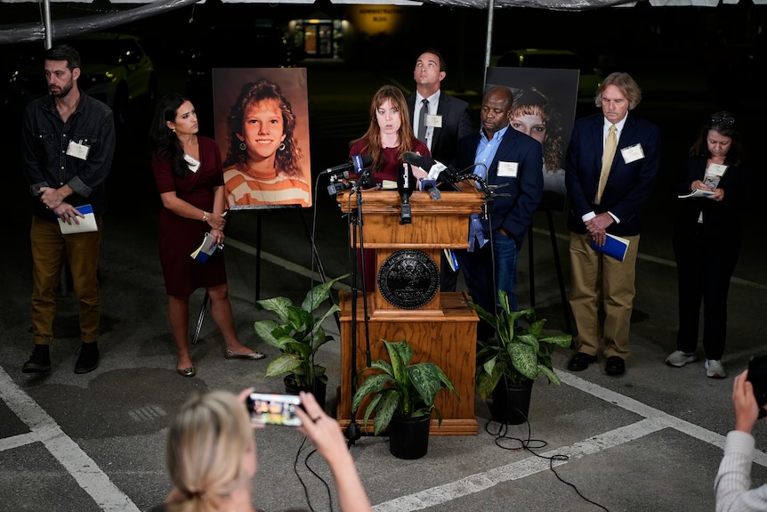 people stand at a podium in front of photos of a teenage girl