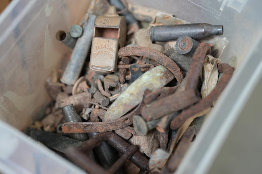 A plastic box containing metal scraps including bullet casings, bridles, nails and a whistle.