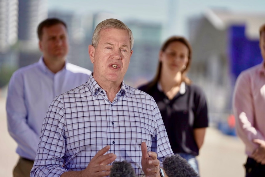 a white middle-aged man standing at a bank of microphones