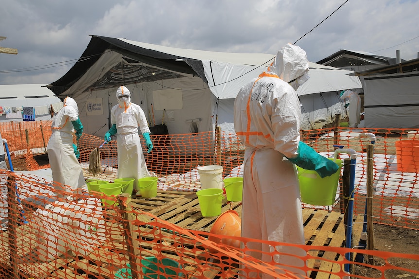 Health workers inside a fenced area in hazmat suits.