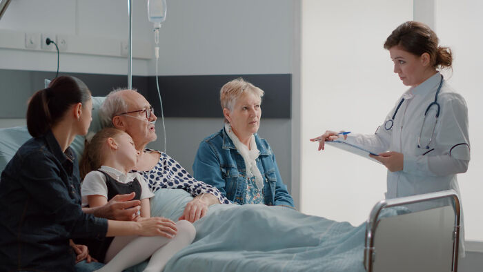 A female doctor speaking with a patient and family in a hospital room, representing doctors and nurses.