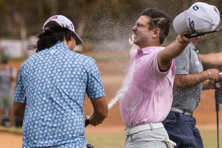 Professional golfer David Micheluzzi holds his arms wide as he is sprayed with champagne in celebration. 
