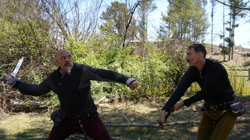 Two men in middle high ages armour engage in a sword fight 