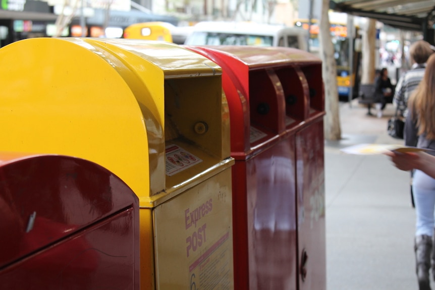 Yellow and red Australia Post boxes lined up on a busy street.